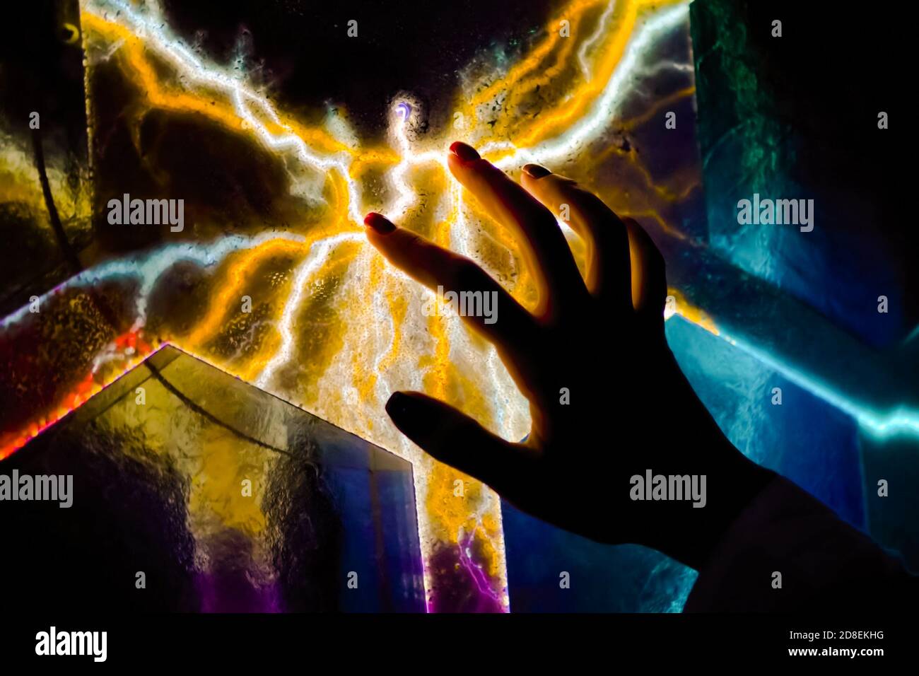Exposition interactive à écran tactile dans le musée des sciences. Femme à la main touchant l'écran plasma coloré dans la pièce sombre - vue rapprochée. Électricité Banque D'Images