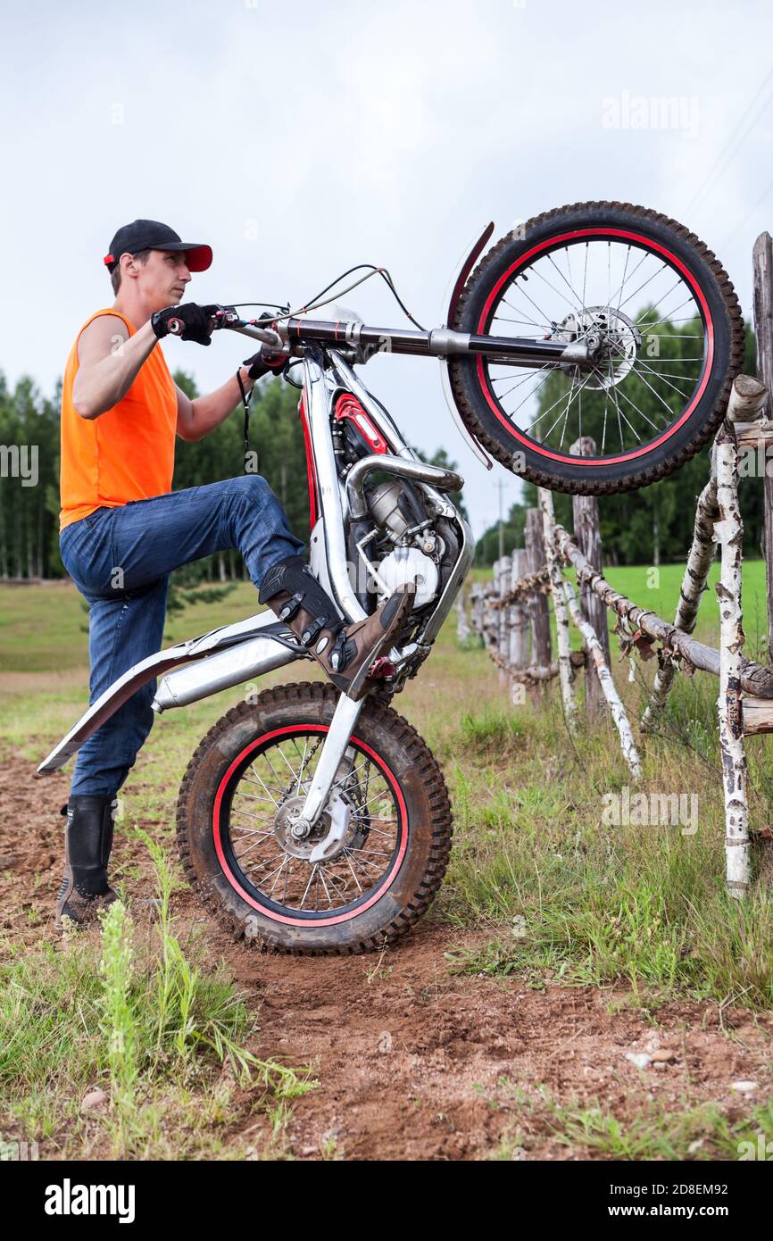 Associé à un essai de mototrcycle d'entraînement dans la campagne, levant le vélo sur la roue arrière, s'appuyant contre la clôture rurale Banque D'Images