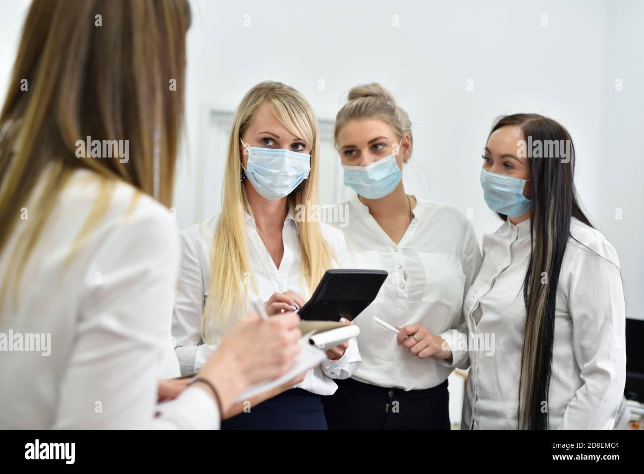 Des femmes de bureau portant des masques lors d'une réunion à le bureau compte les dépenses sur une calculatrice Banque D'Images
