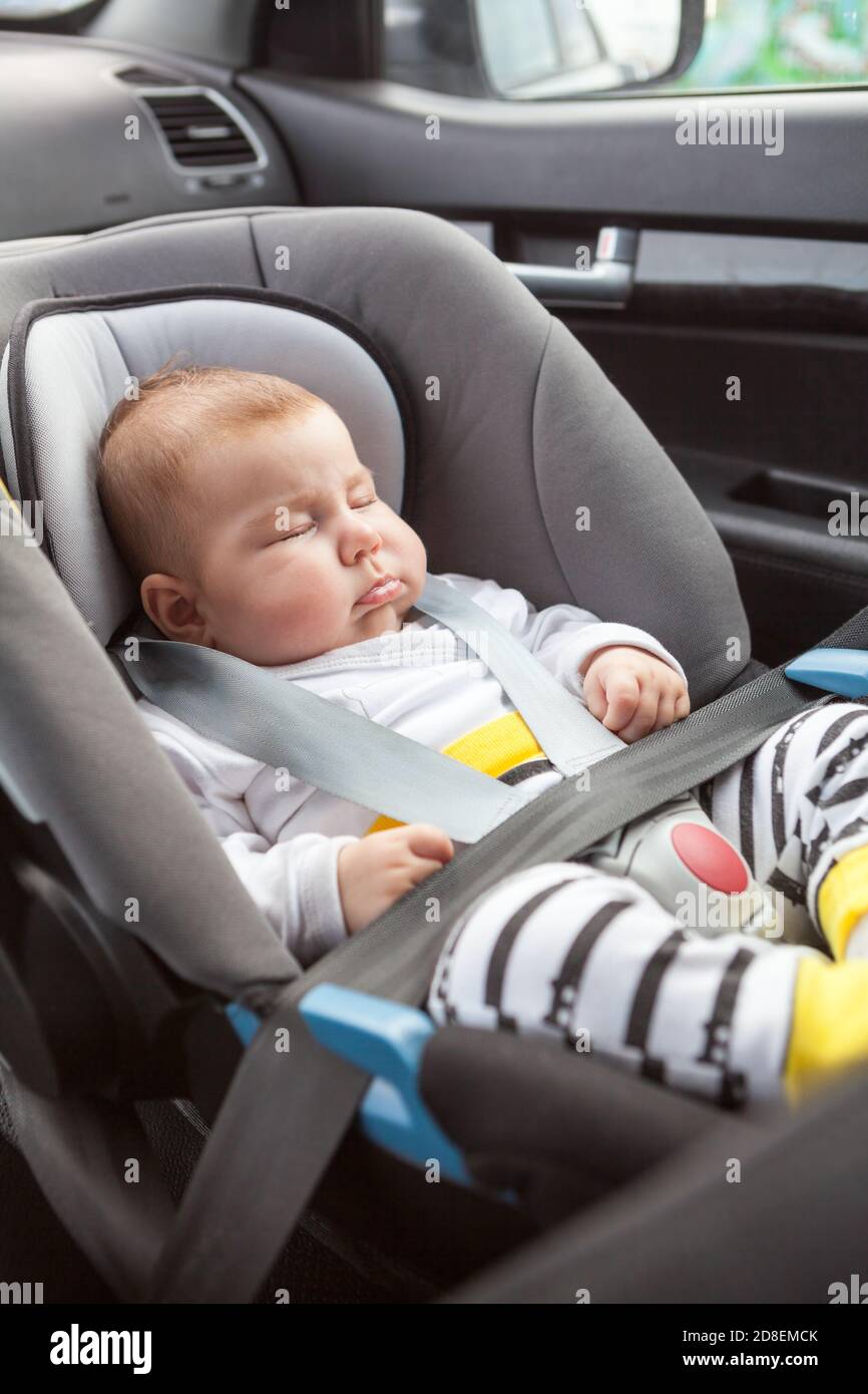 Enfant nouveau-né dormant sur le siège de sécurité de la voiture, attachez-le avec les ceintures sur la chaise du passager avant Banque D'Images