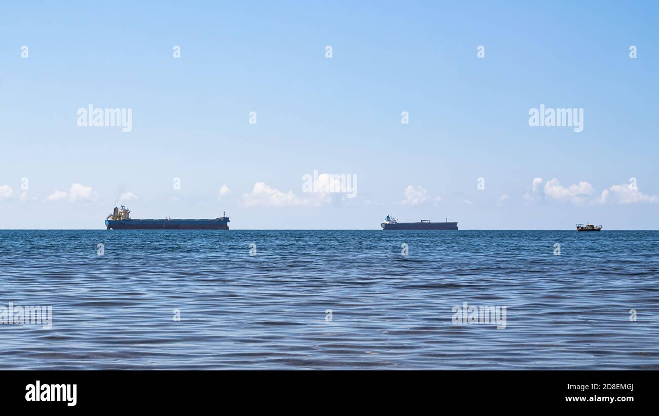 Gros plan sur un paysage marin minimaliste lors d'une belle journée d'été. Mer bleue, nuages à l'horizon et plusieurs navires de cargaison Banque D'Images