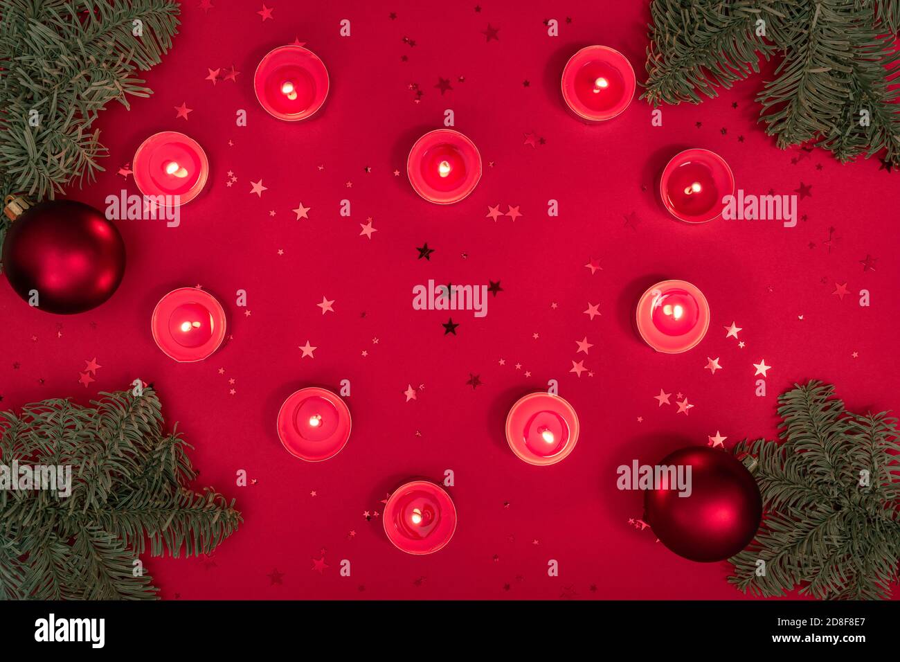 Noël romantique composition du soir faite de bougies en feu, branches d'arbre, paillettes et boules sur la surface rouge. Joyeux noël et heureux 2021 Banque D'Images