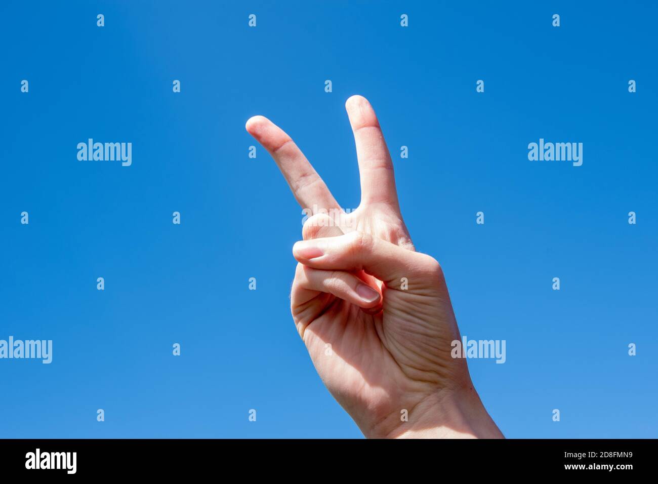 Symbole de mouvement numéro deux. Deux doigts d'une main de femme caucasienne montrant la victoire ou le geste de paix sur le ciel bleu Banque D'Images