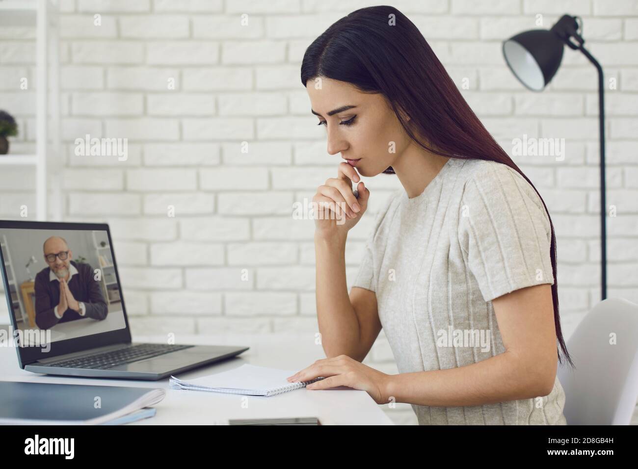 Femme assise avec un ordinateur portable et un ordinateur portable et prenant des notes pendant cours en ligne avec professeur Banque D'Images