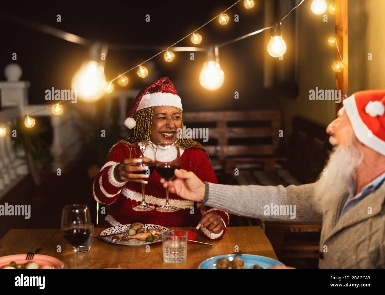 De joyeux amis multiraciaux âgés de griller avec des verres à vin rouge pendant Fêtes de Noël dîner sur le patio maison fête Banque D'Images