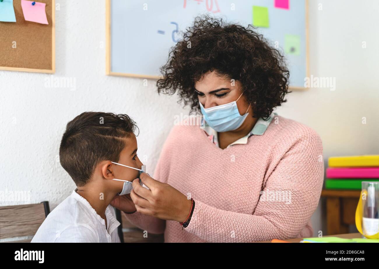 La femme enseignante a mis un masque de protection du visage à l'élève en préscolaire Salle de classe pendant la pandémie de virus corona - concept de soins de santé et d'éducation Banque D'Images