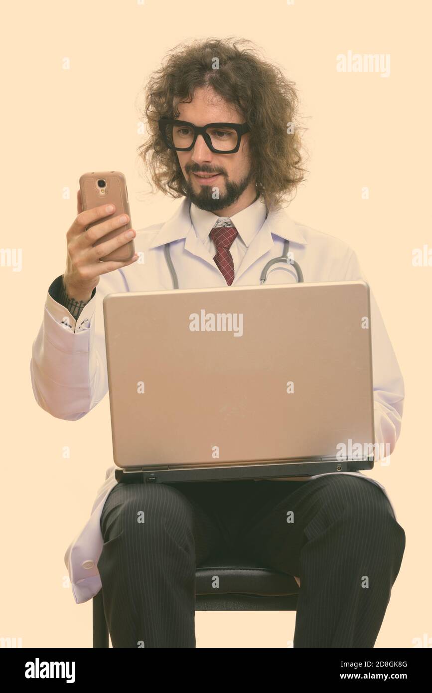 Homme heureux doctor smiling tout en utilisant le téléphone mobile à l'ordinateur portable Banque D'Images