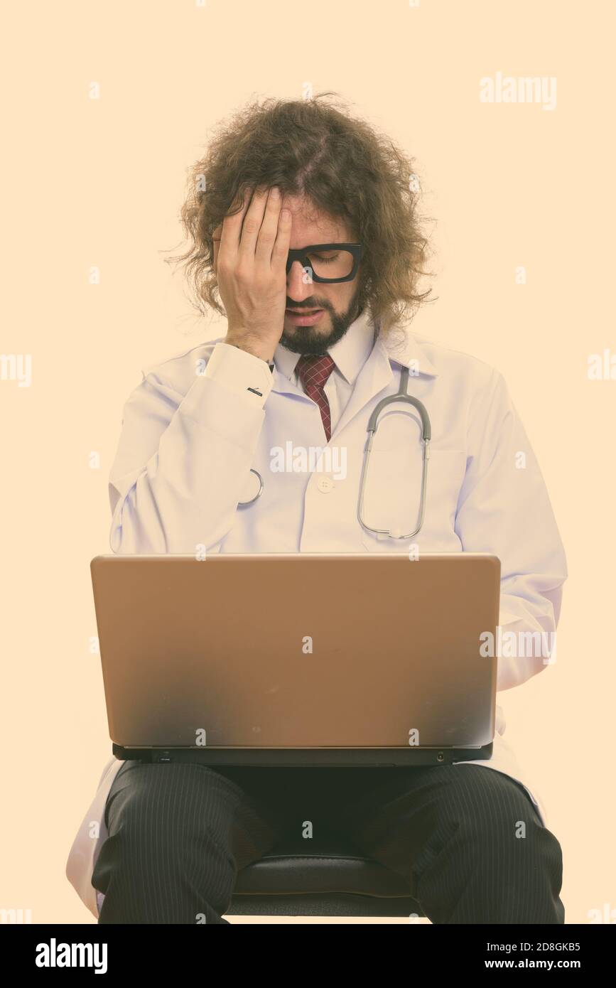 Studio shot of a souligné l'homme médecin using laptop while covering face Banque D'Images