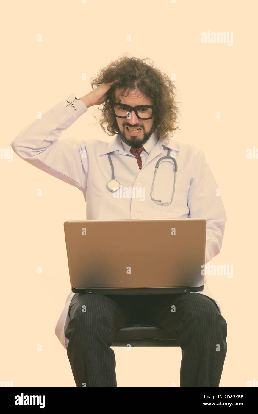 Studio shot of a souligné l'homme médecin à l'aide d'un ordinateur portable avec main sur sa tête Banque D'Images