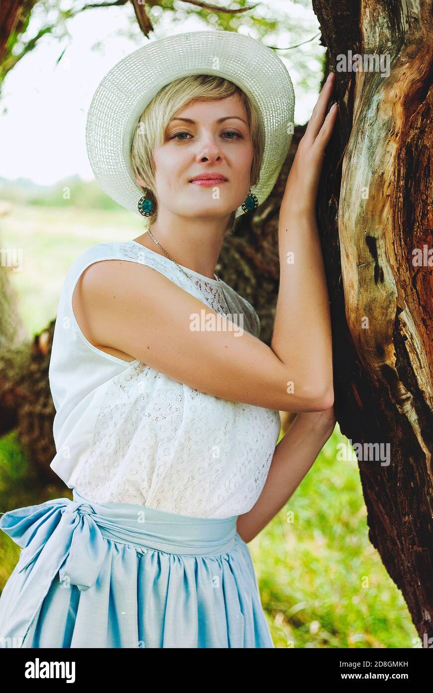 Jeune femme heureuse élégante avec chapeau en vêtements vintage marchant seul dans la nature dans le champ vert. Banque D'Images