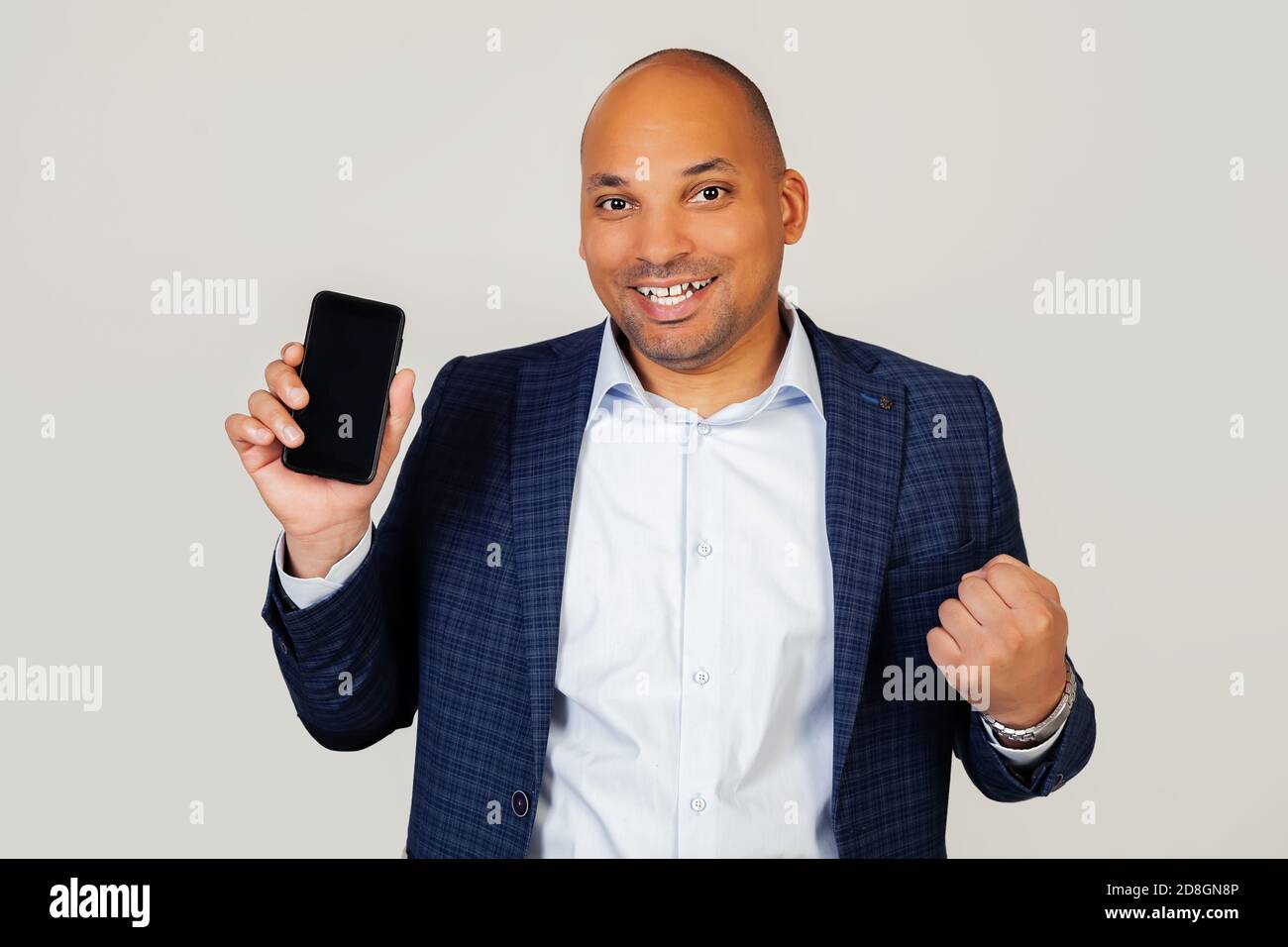 Portrait du jeune homme d'affaires afro-américain heureux, montre l'écran de smartphone, crie avec fierté et célèbre la victoire et le succès, très excité, se réjouit des émotions. Debout sur un fond gris Banque D'Images