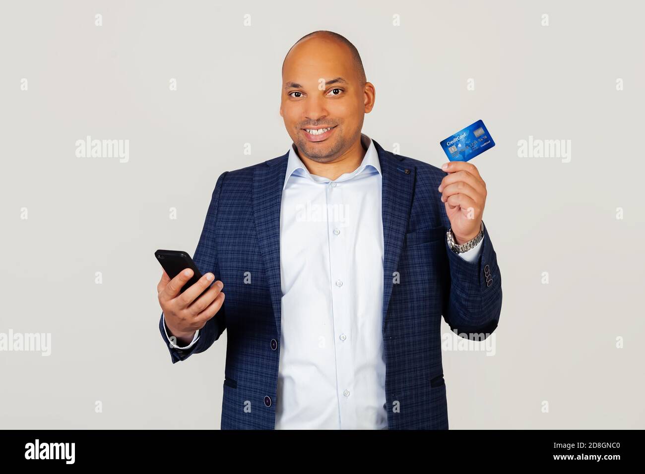 Portrait d'un jeune homme d'affaires afro-américain heureux utilisant une carte de crédit pour payer en ligne à l'aide d'un smartphone. Debout sur un fond gris Banque D'Images