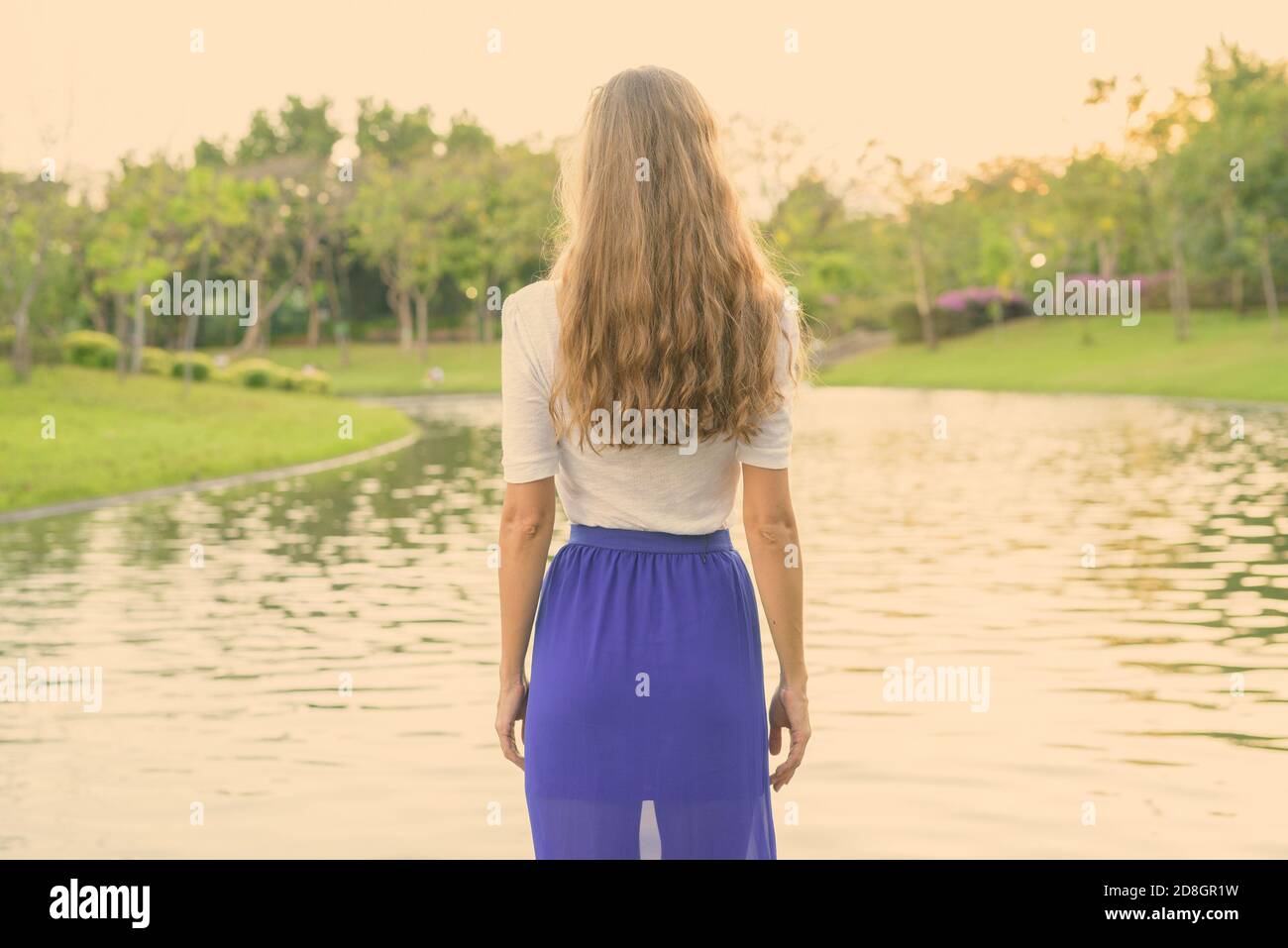 Belle femme aux cheveux longs et permanent à la recherche en vue panoramique sur le lac dans le parc verdoyant paisible Banque D'Images