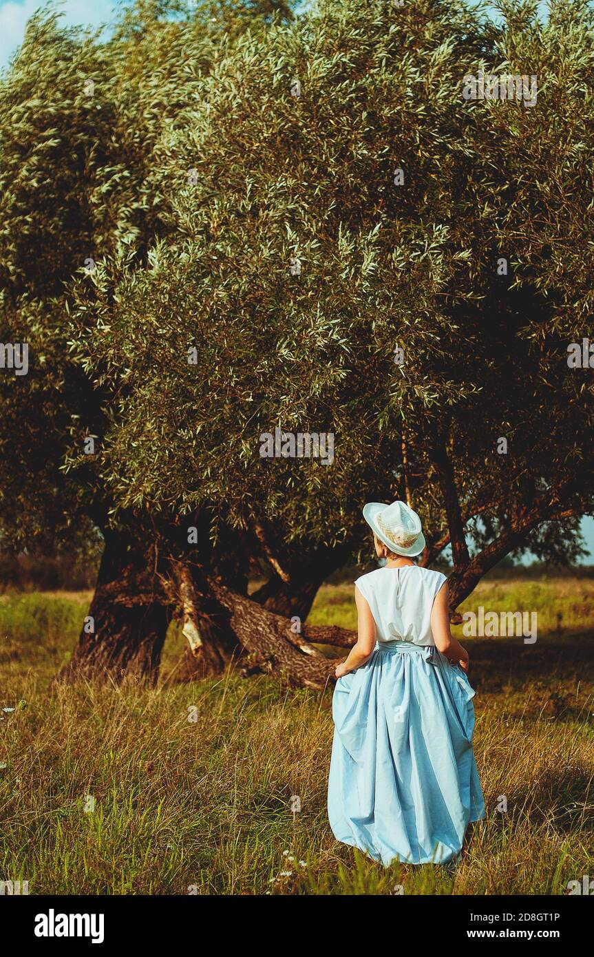 Jeune femme heureuse élégante avec chapeau en vêtements vintage marchant seul dans la nature dans le champ vert. Banque D'Images