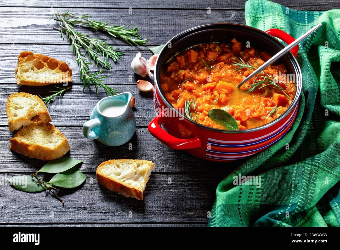 Soupe de potiron saine et à base de keto dans une casserole rouge avec une cuillère à verser sur un fond en bois avec pain grillé, crème, ail, feuille de Laurier, romarin, dessus Banque D'Images