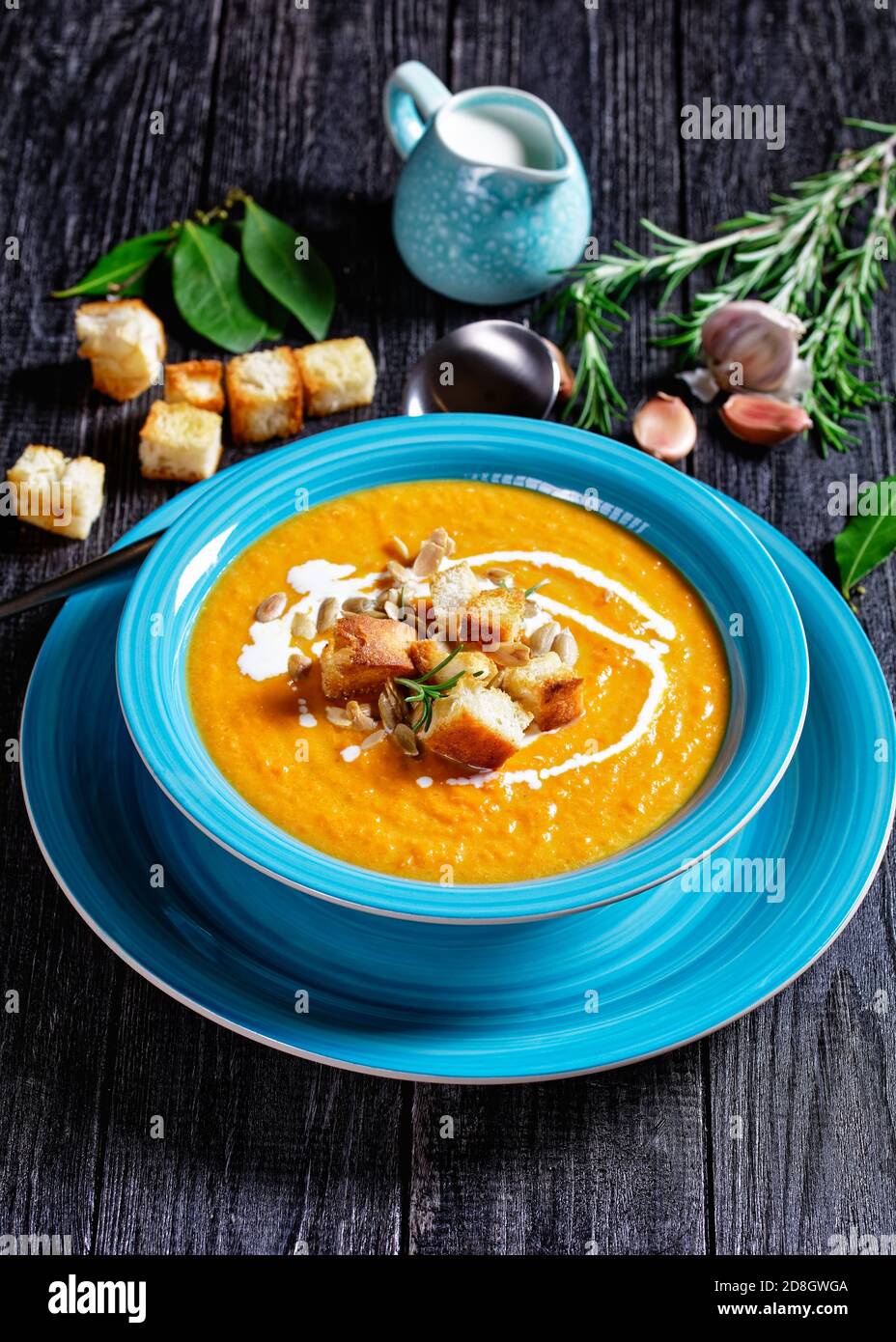 Soupe de potiron crémeuse et réconfortante à l'automne dans une assiette bleue avec des croûtons et des graines de potiron sur un dessus sur un fond en bois sombre avec de la crème, de l'ail, de la ba Banque D'Images