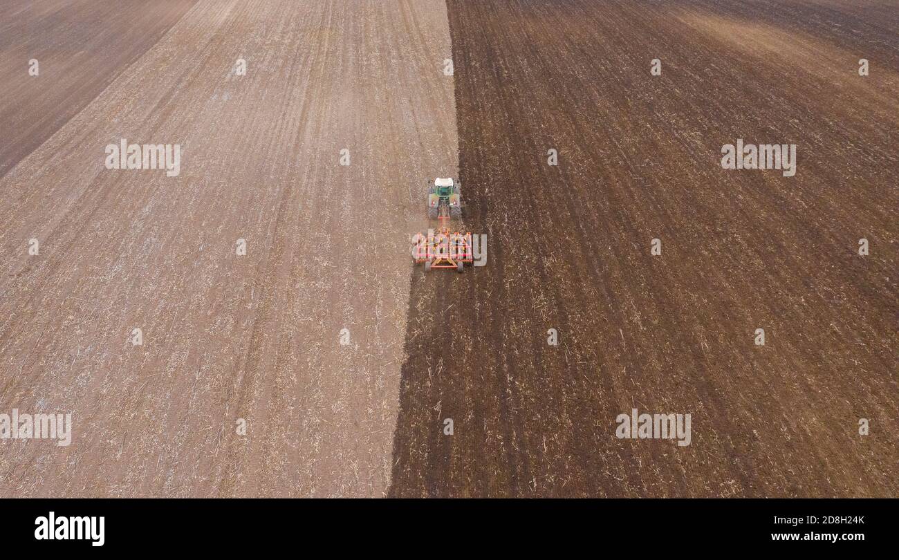 Lajoskomarom, Hongrie - vue aérienne des tracteurs rouges cultivant des champs à la campagne après la récolte. Concept agricole, travaux agricoles sur les terres agricoles. Banque D'Images