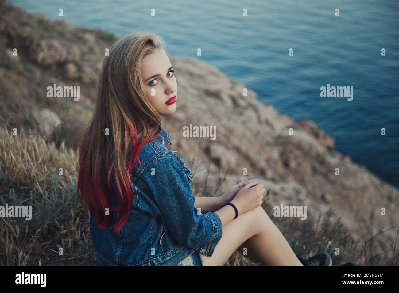 Portrait d'une jeune fille en face de la mer dans des vêtements élégants avec coiffure et maquillage. Arrière-plan flou à des fins artistiques. Banque D'Images