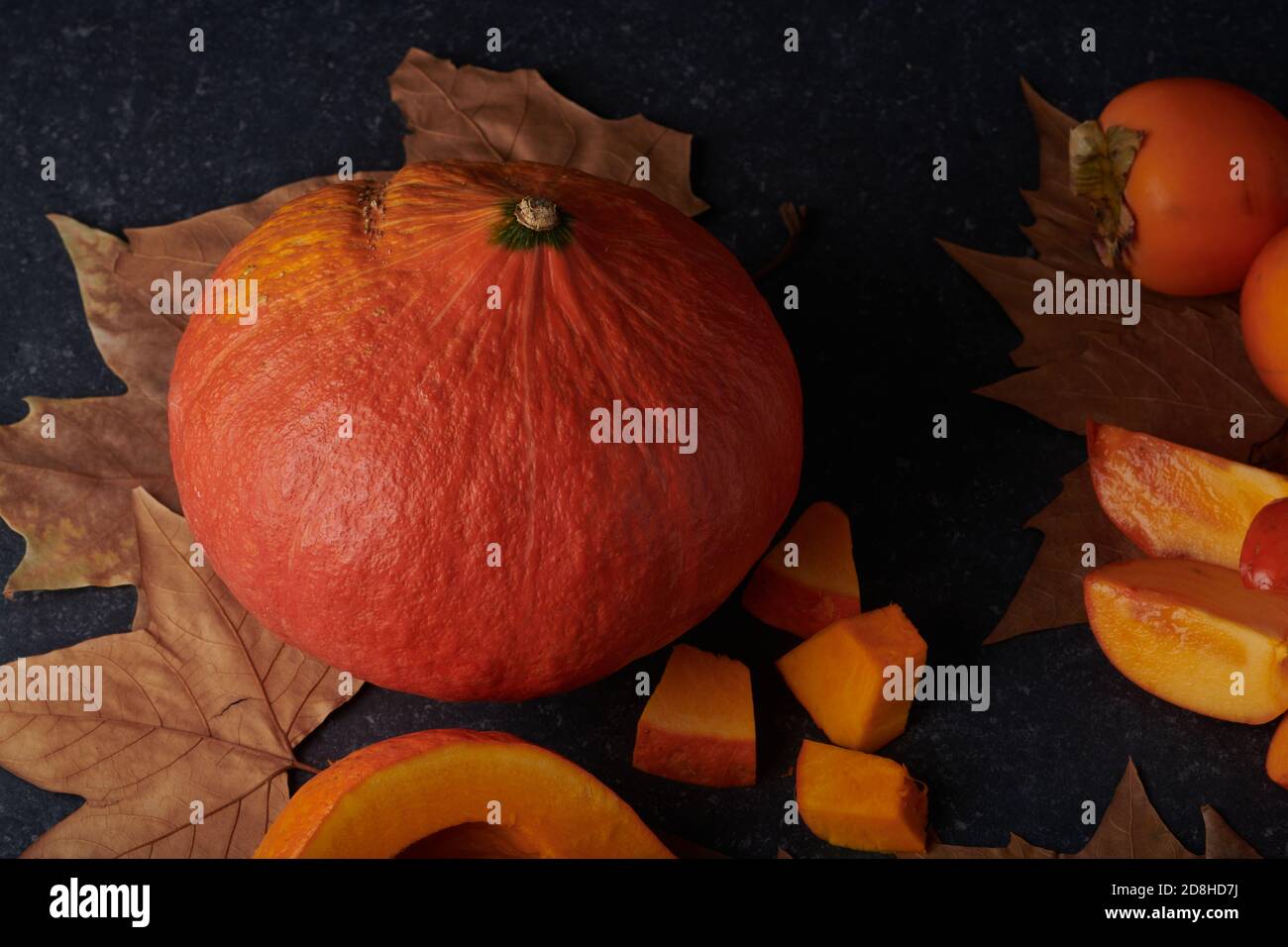 Citrouille entière et morceaux frais crus sur fond de pierre avec feuilles d'automne Banque D'Images