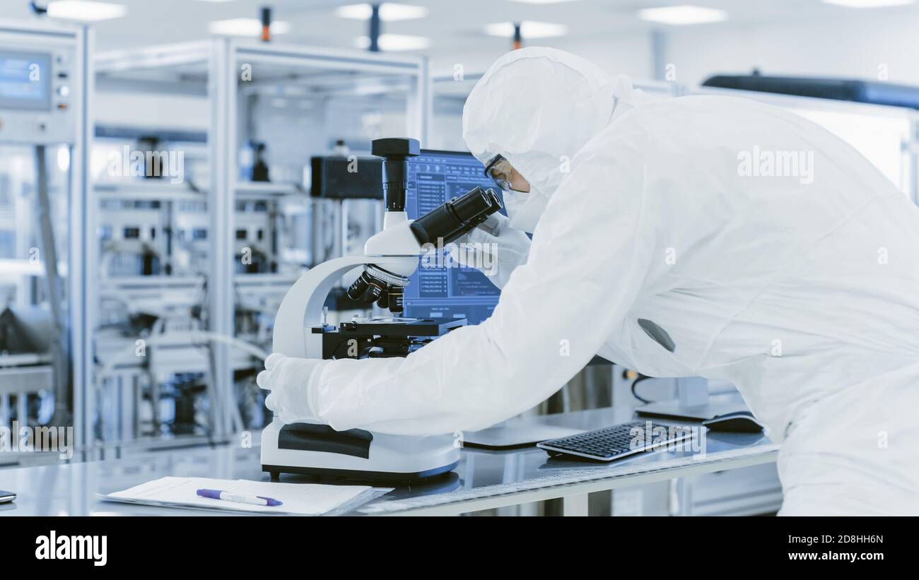 En laboratoire scientifique en vêtements de protection faire de la recherche utilise le microscope et l'ordinateur personnel. Manufactory moderne produisant des semi-conducteurs et Banque D'Images
