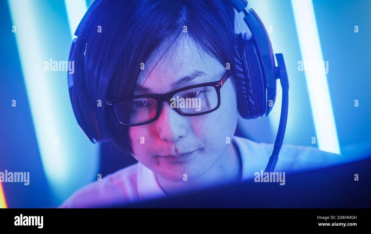 Joueur professionnel d'Asie de l'est jouant dans le jeu vidéo en ligne sur son ordinateur personnel. Donne des commandements à son équipe utilise le microphone. Salle éclairée par Neon Banque D'Images