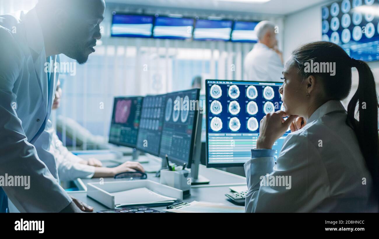 Deux scientifiques du laboratoire de recherche sur le cerveau travaillent. Les neurologues utilisent un ordinateur personnel avec l'IRM, les scannages CT montrent des images du cerveau. Banque D'Images