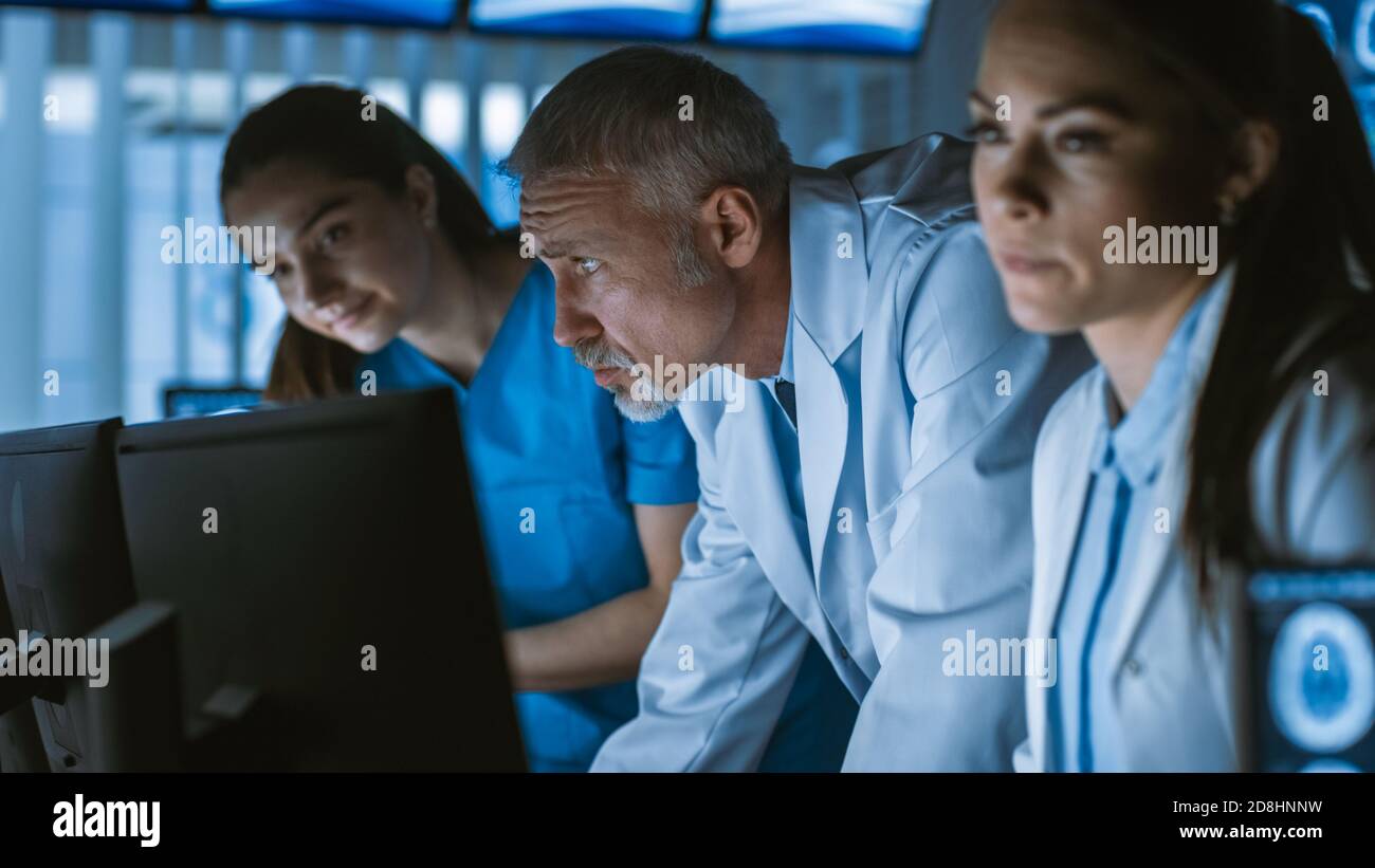 Une équipe diversifiée de scientifiques médicaux résolvent les problèmes et pointez sur les écrans d'ordinateur montrant les scannages CT et IRM. Neurologues neuroscientifiques travaillant dans le cerveau Banque D'Images