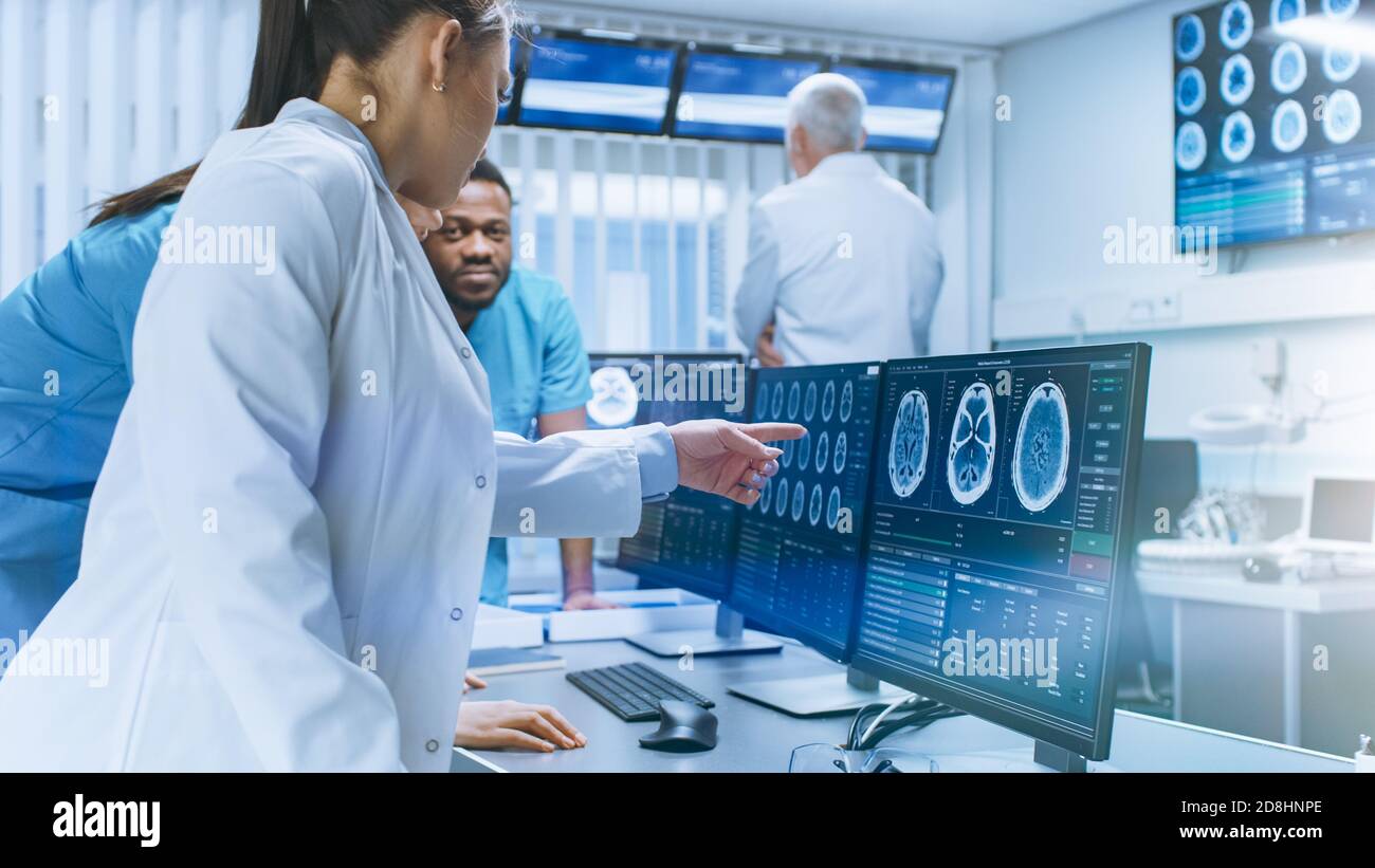 Une équipe diversifiée de scientifiques médicaux résolvent les problèmes et pointez sur les écrans d'ordinateur montrant les scannages CT et IRM. Neurologues neuroscientifiques travaillant dans le cerveau Banque D'Images
