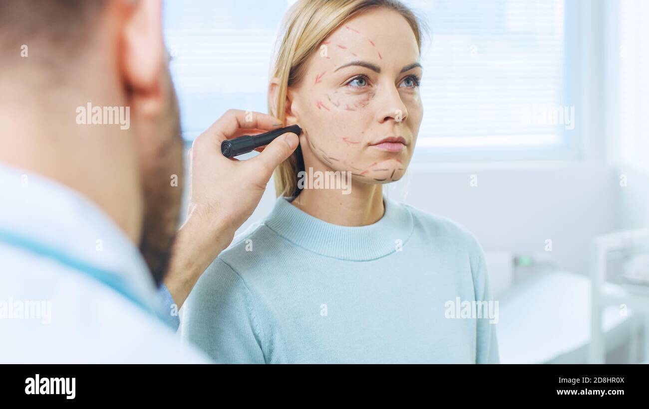 Prise de vue au-dessus de l'épaule d'une patiente assise patiemment tandis que le chirurgien plasticien dessine des lignes sur son visage pour l'opération de Facelift. Banque D'Images