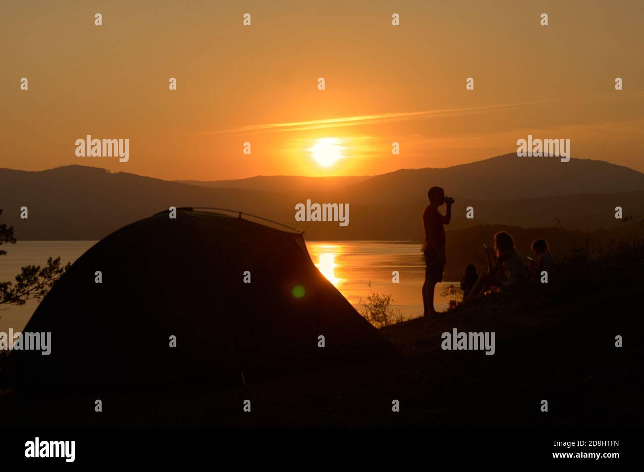 Silhouette de groupe de personnes et tente touristique contre le coucher de soleil sur le lac. Faites la fête avec un verre. Profitez du camping de voyage Banque D'Images