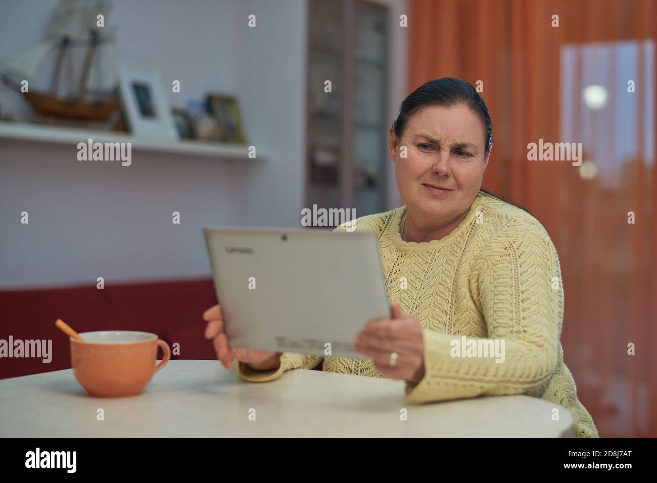 Femme âgée en chandail jaune regardant un ordinateur portable avec un visage malheureux Banque D'Images