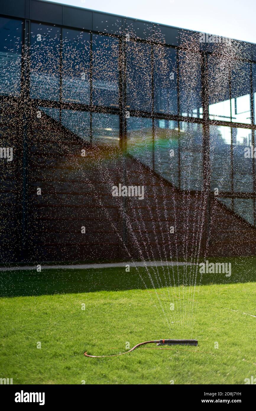 Arroseur d'eau sur la pelouse à l'extérieur d'un bâtiment public avec un arc-en-ciel Banque D'Images