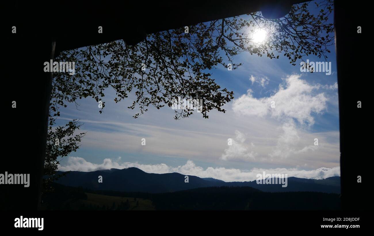 Vue par une fenêtre depuis une maison en bois dans l' forêt avec le soleil dans le ciel entouré de nuages Et avec la Forêt Noire en arrière-plan Banque D'Images