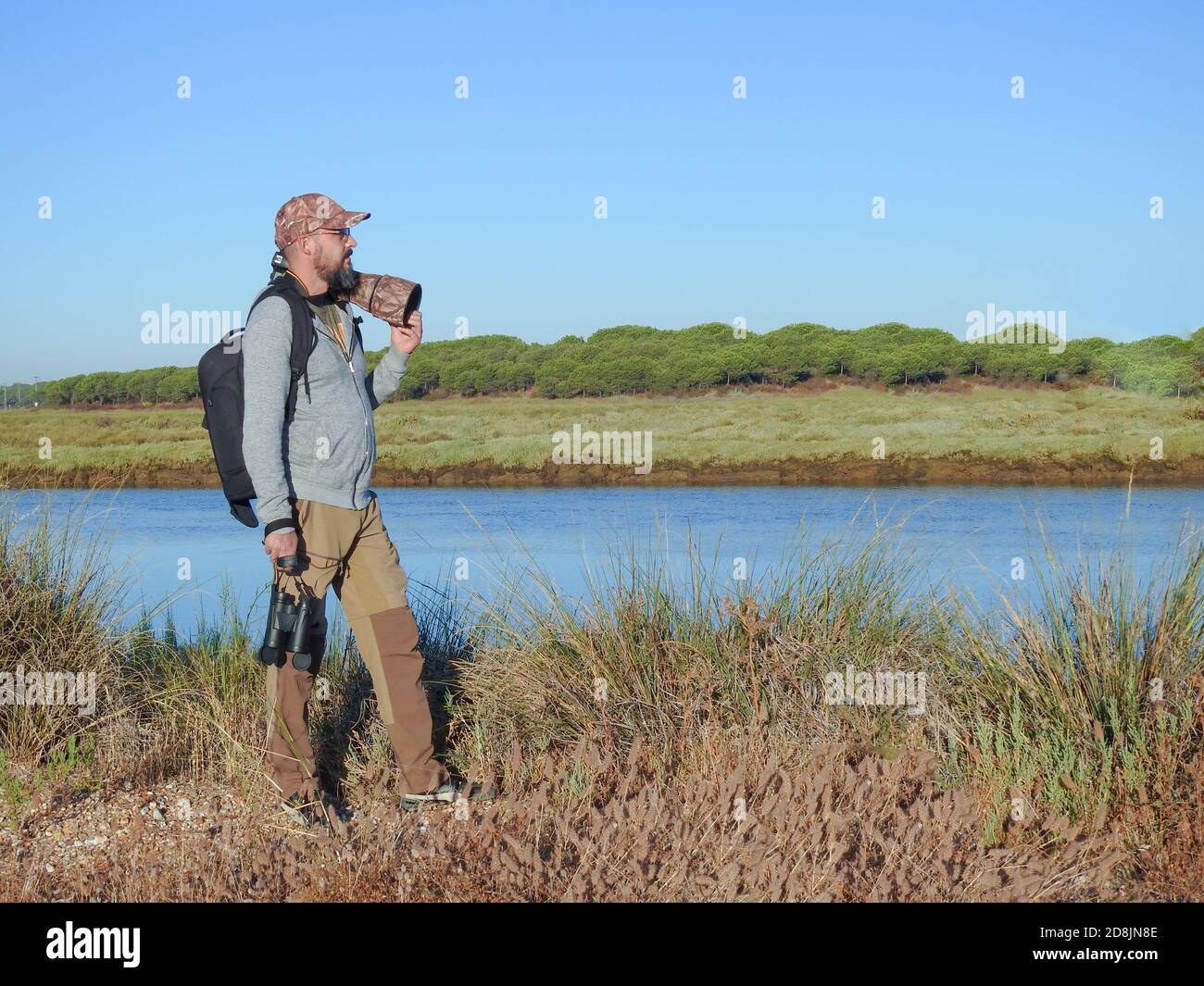 jeune homme hippster avec une barbe sur le terrain, portant un équipement photographique avec un appareil photo reflex, un téléobjectif, des jumelles et un sac à dos Banque D'Images