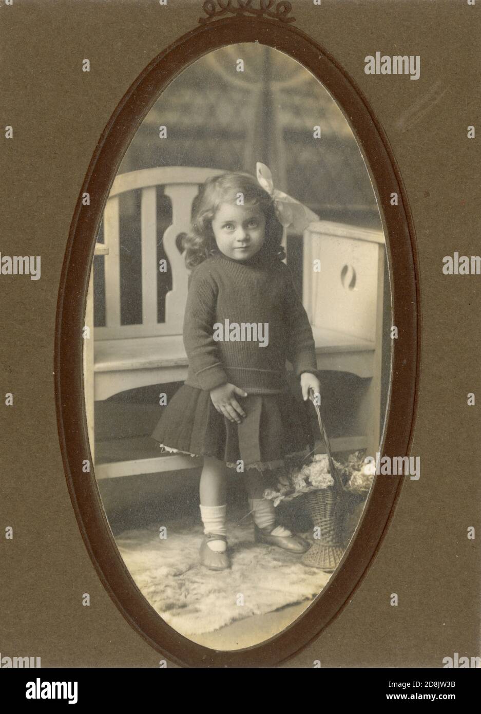Début des années 1900, Edwardian studio portrait photographie dans le support ovale de la jeune fille mignon tenant un panier de fleurs, à côté d'un banc blanc, Royaume-Uni vers 1910 Banque D'Images
