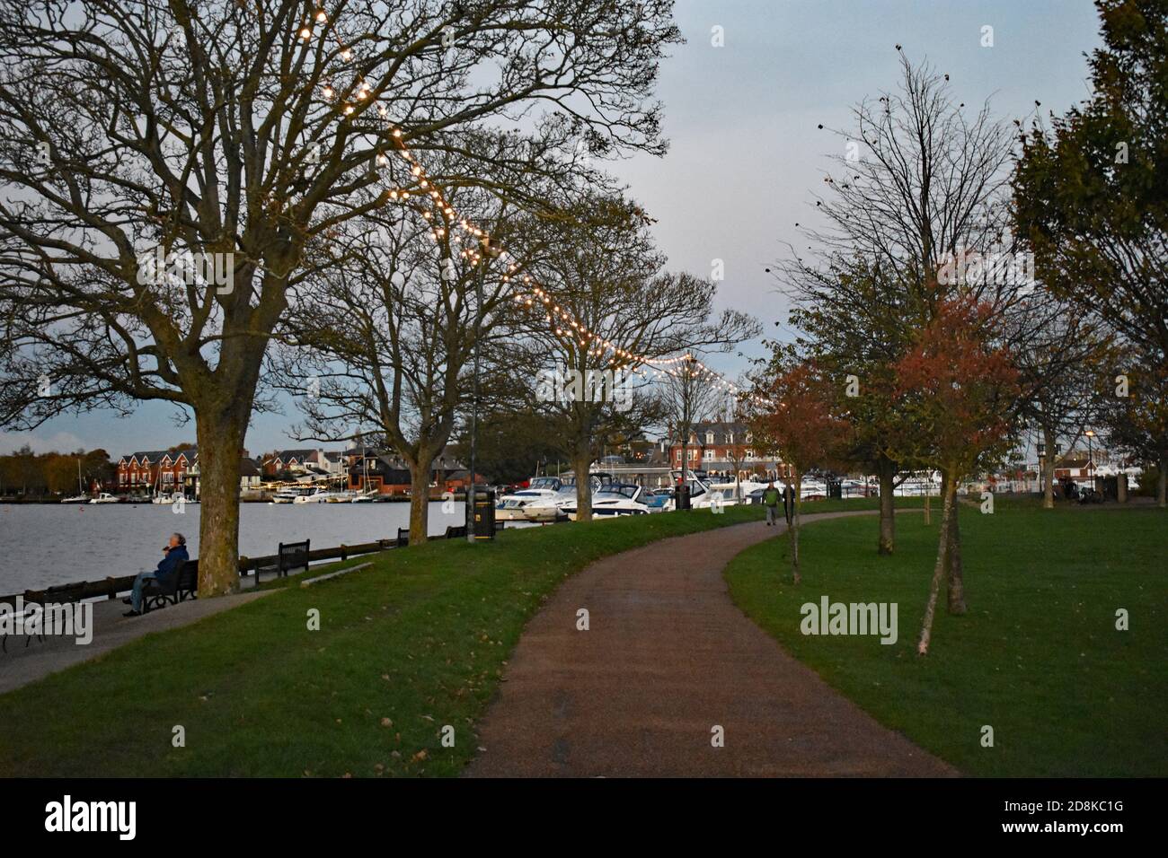 Un chemin bordé d'arbres se dirigeant vers la marina le long du bord de Oulton Broad près de Lowestoft dans le parc national de Broads, en Angleterre. Banque D'Images