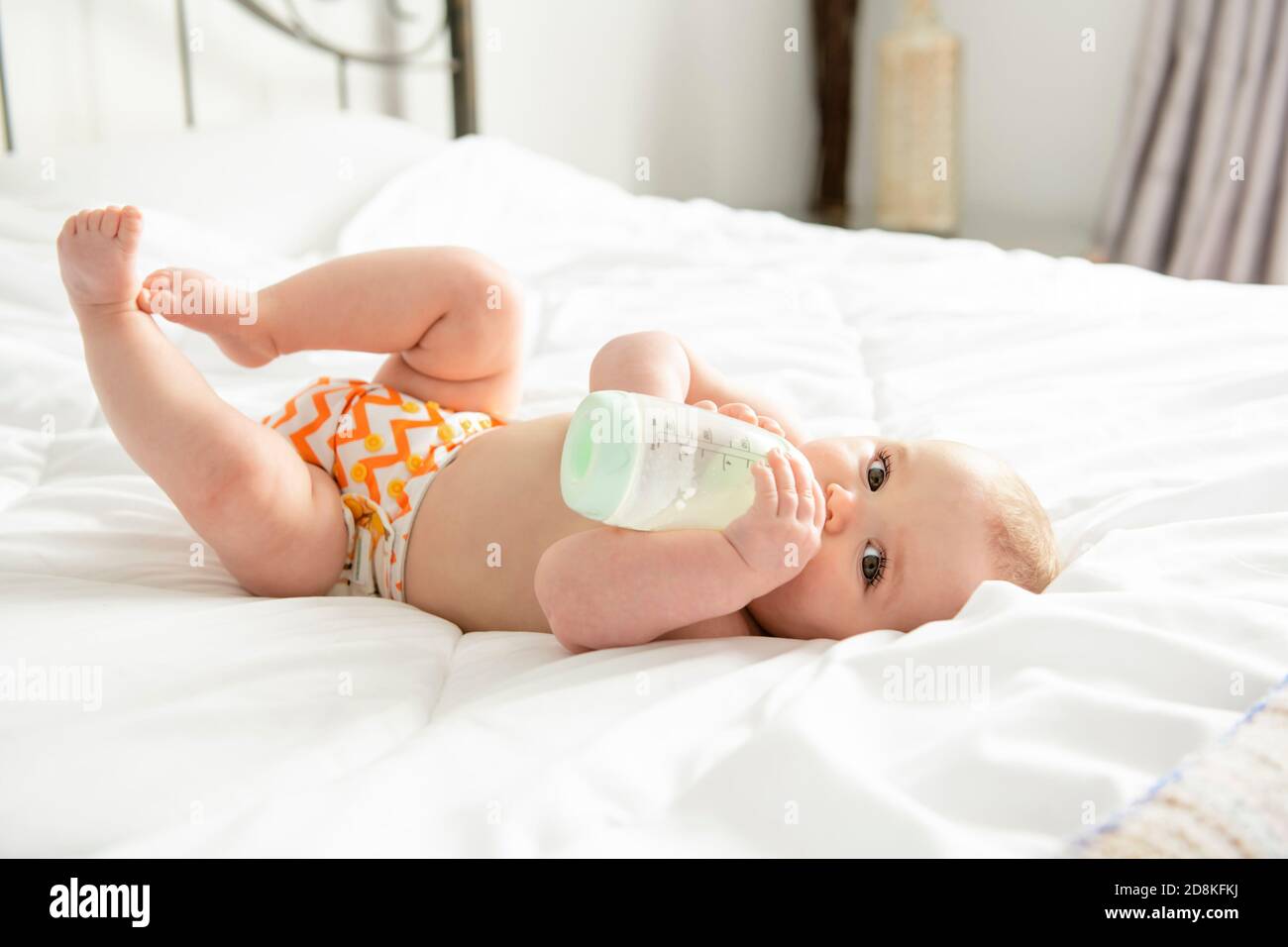 Une jolie petite fille boit du lait dans un biberon allongé sur le lit.  Enfant couche dans la chambre de bébé Photo Stock - Alamy