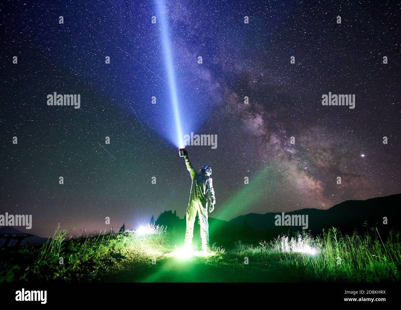 Spaceman porte une combinaison d'espace blanche et un casque dirige un  rayon de lumière bleu dans le ciel plein d'étoiles avec une lanterne dans  la nuit dans les montagnes, debout sur l'herbe