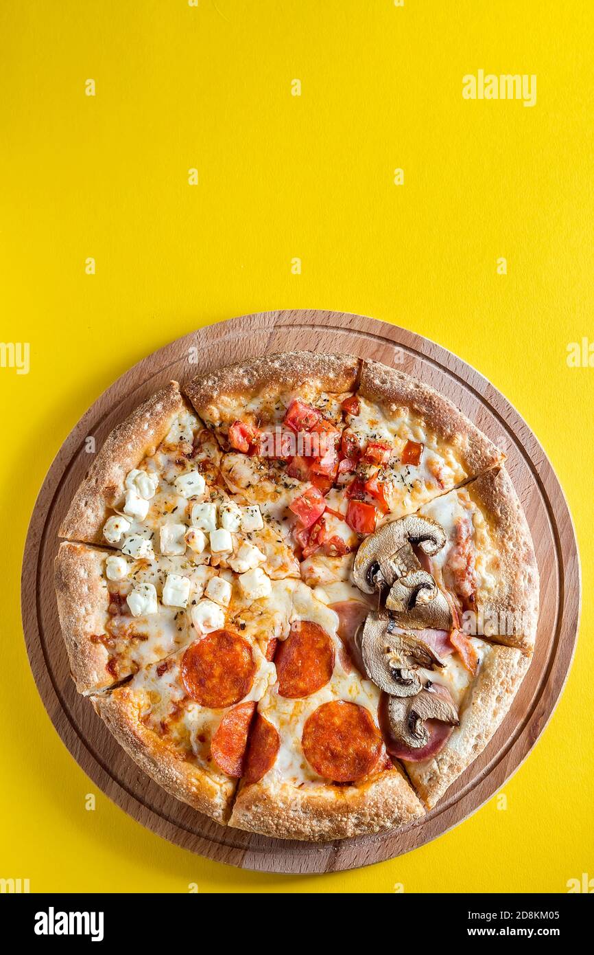 La pizza est sur une planche à découper en bois sur fond jaune vif. Quatre saveurs différentes de pizza. Espace pour le texte. La vue du dessus. Banque D'Images