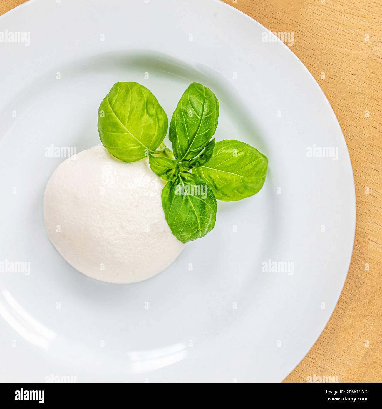 Fromage Mozzarella italien traditionnel et feuille de basilic sur une assiette blanche sur une table en bois. Cuisine italienne traditionnelle Banque D'Images