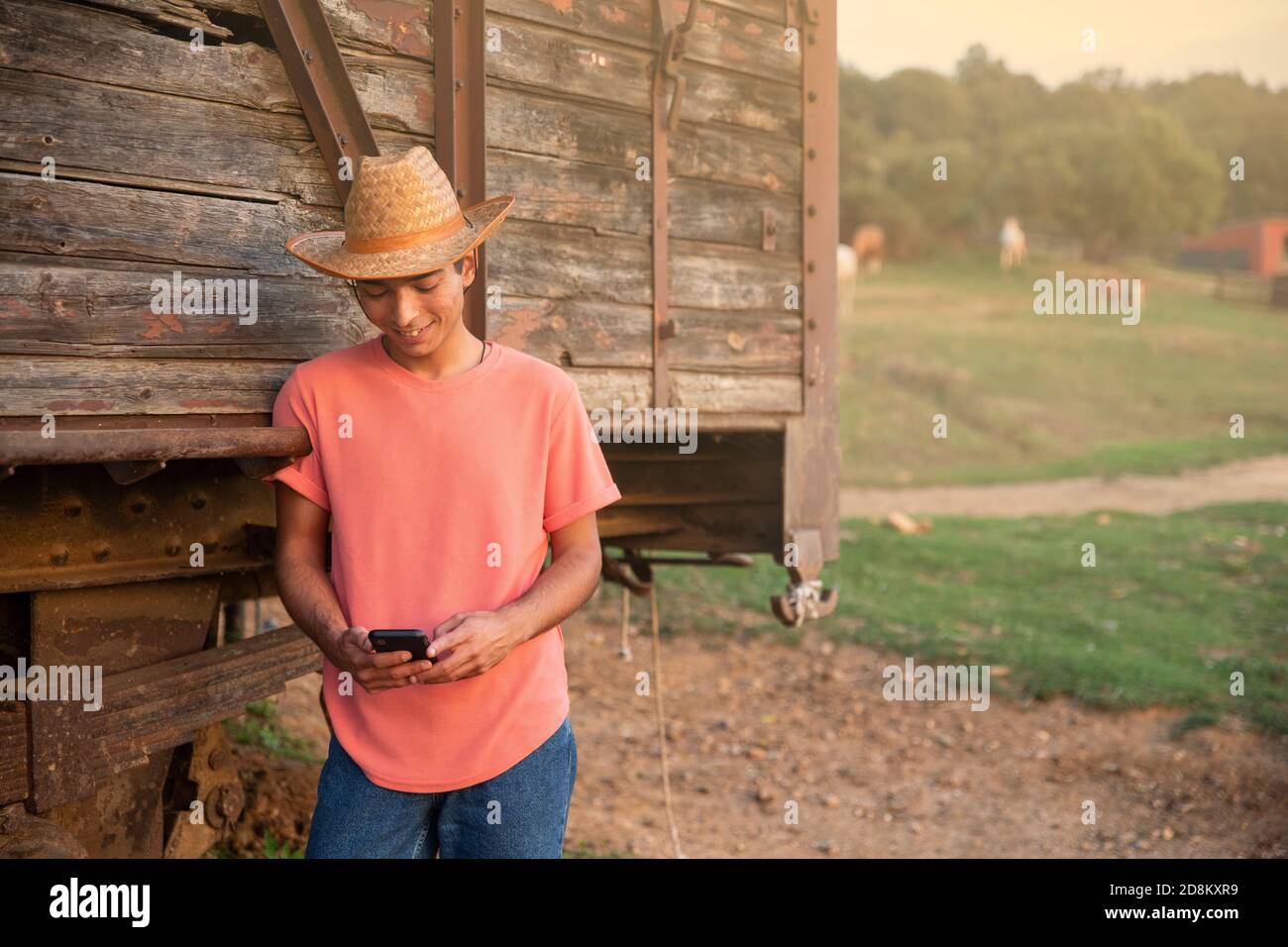 Jeune homme avec un chapeau de cowboy regardant le coucher de soleil devant un train en bois Vintage Wagon. Ranch concept Photographie Banque D'Images