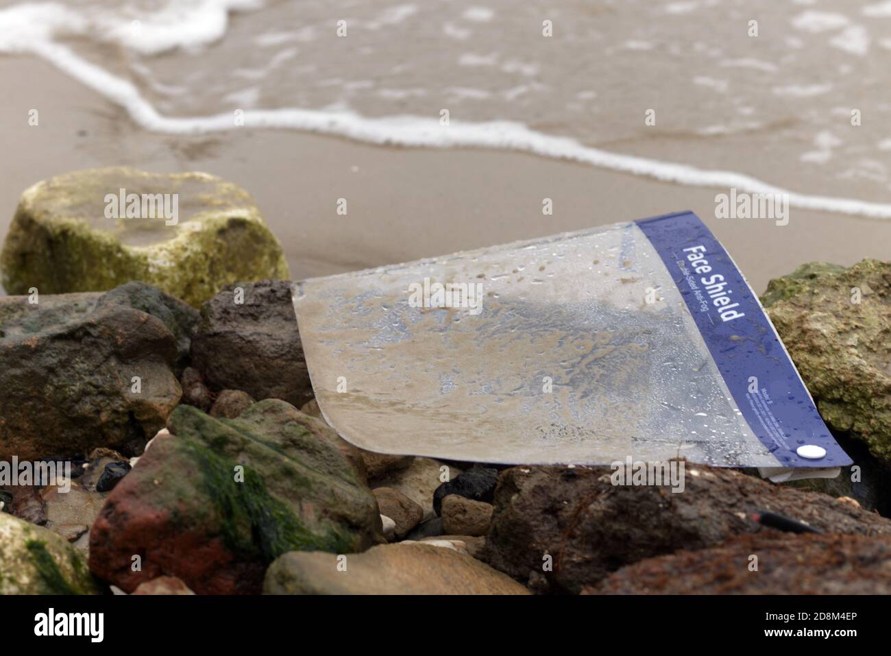 Un écran facial jeté et lavé sur la plage, causant un problème environnemental avec les déchets de plastique pendant la pandémie. Banque D'Images