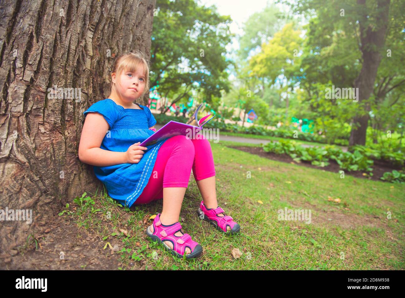 Un portrait de trisomie 21 enfant fille dehors ayant le plaisir sur un livre de lecture de parc Banque D'Images
