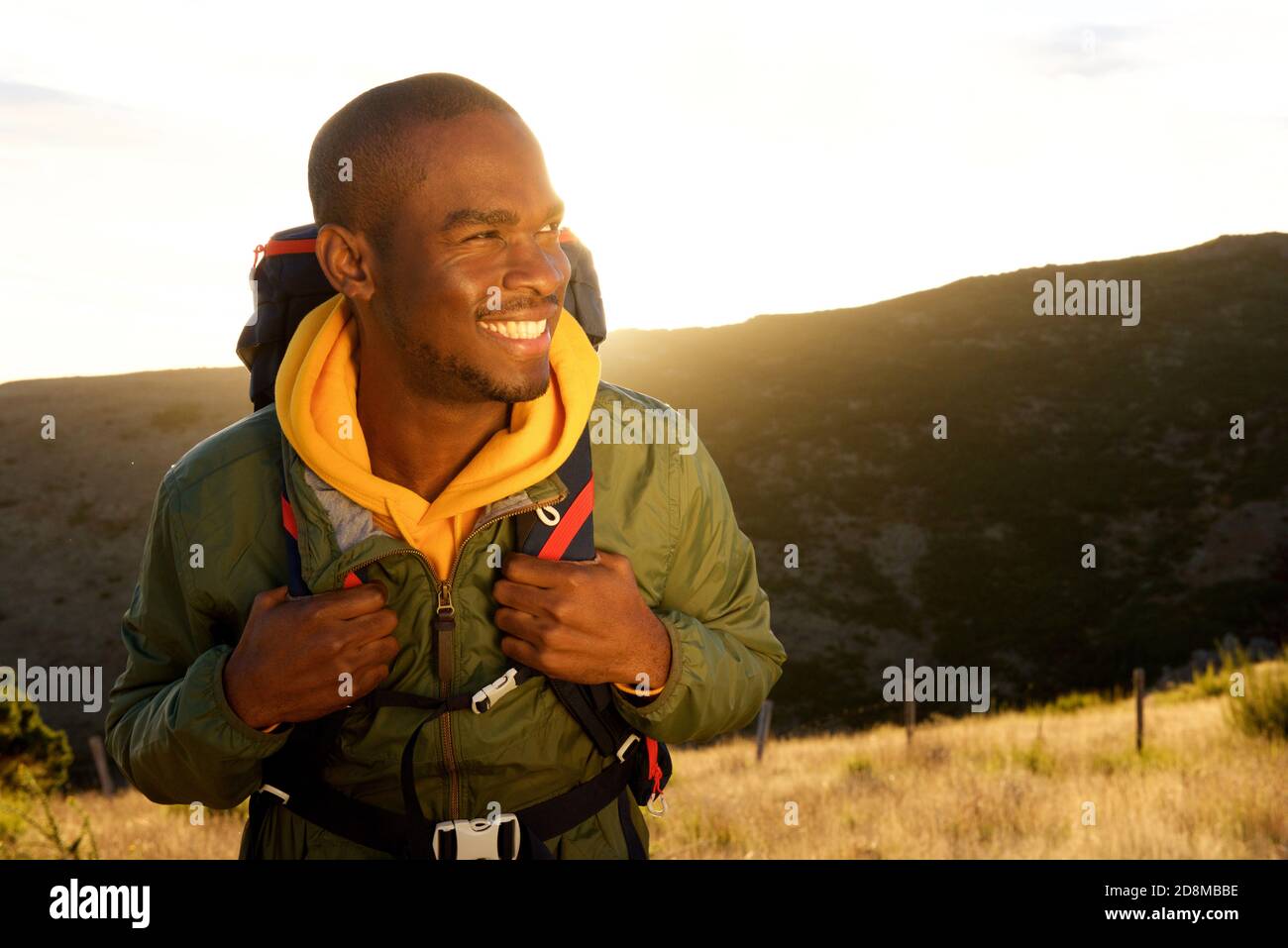 Portrait en gros plan du beau jeune africain américain avec sac à dos souriant avec coucher de soleil en arrière-plan Banque D'Images