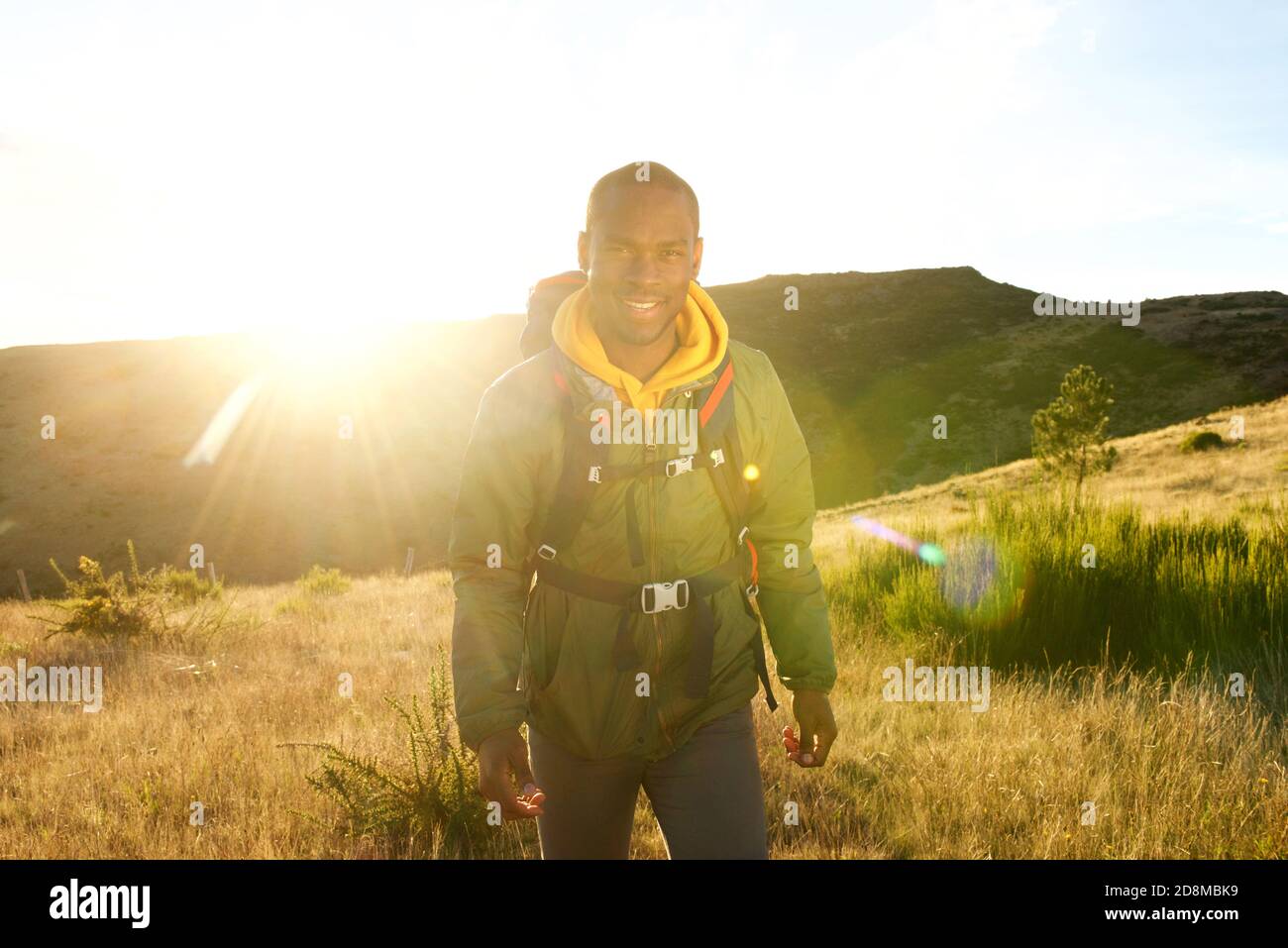 Portrait d'un heureux africain américain marchant dans la nature avec sac à dos et coucher de soleil en arrière-plan Banque D'Images