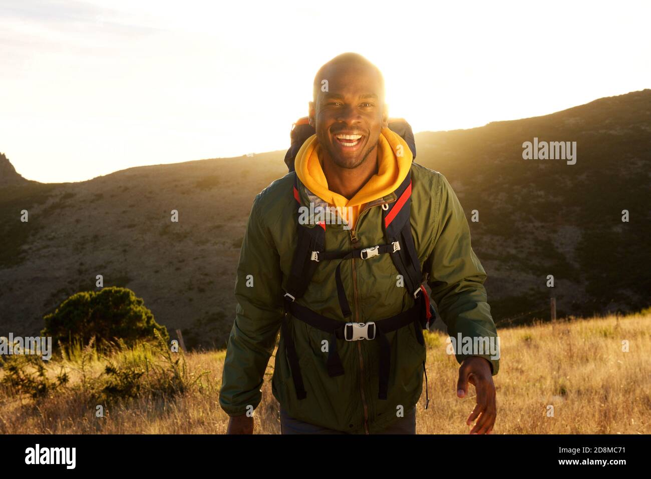Portrait d'un homme afro-américain heureux qui marche dans un sac à dos en montagne et coucher de soleil en arrière-plan Banque D'Images
