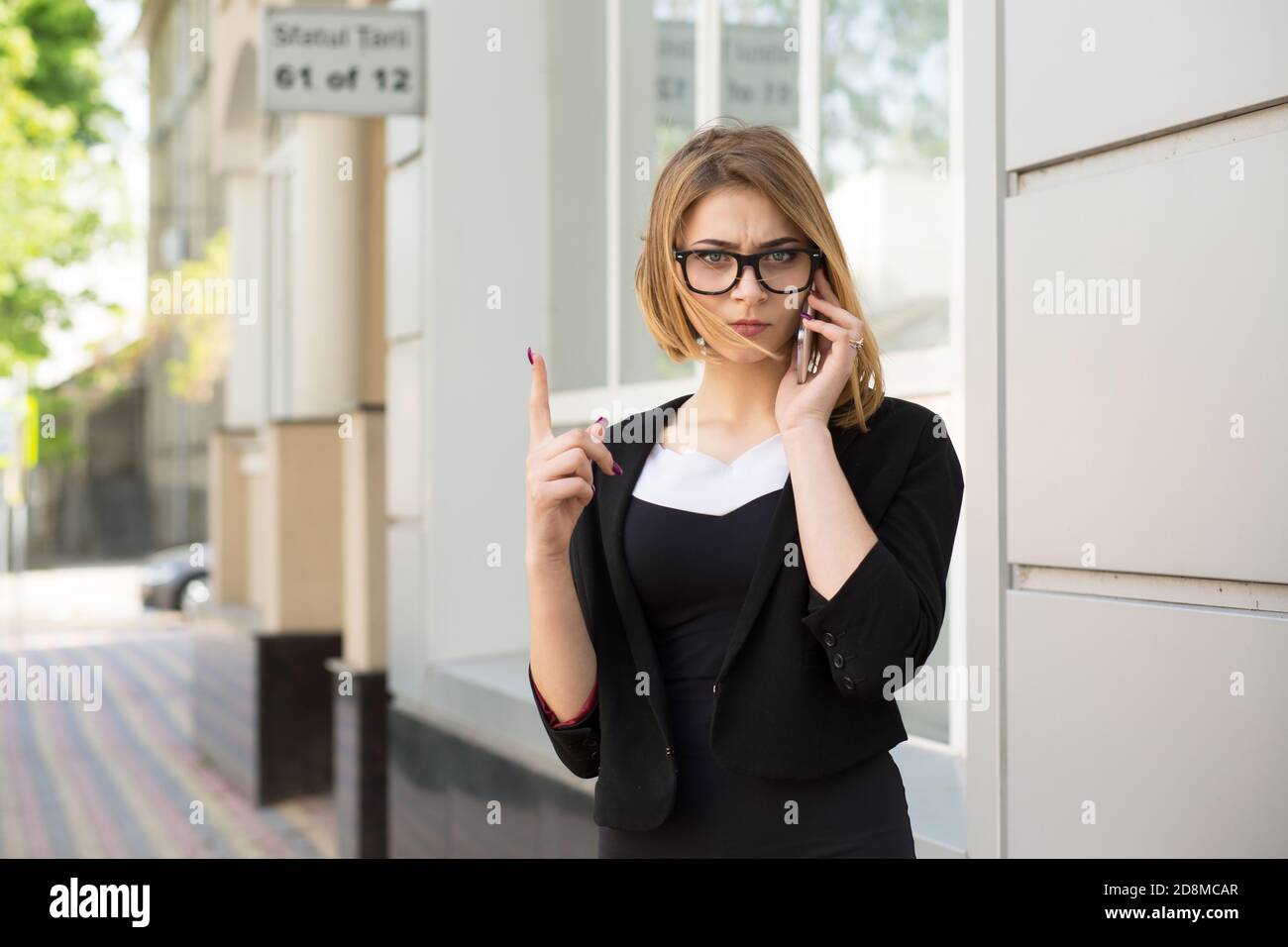 Jeune femme stricte avec smartphone montrant non, ne pas, attention avec le doigt mouvement de la main à l'extérieur près de la maison de bureau magasin. Parler avec les enfants, les parents Banque D'Images