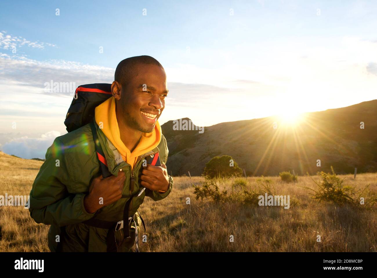 Portrait d'un jeune homme noir marchant avec sac à dos dans les montagnes avec lever du soleil en arrière-plan Banque D'Images