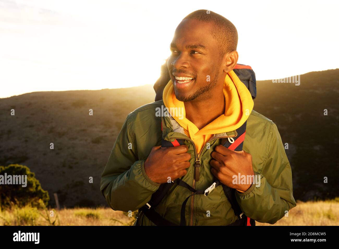 Portrait en gros plan du beau jeune africain américain avec sac à dos souriant avec lever de soleil en arrière-plan Banque D'Images