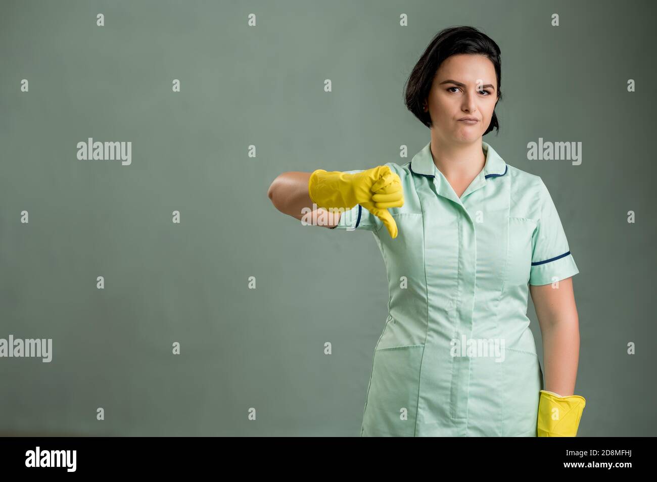 Jeune femme de ménage portant une chemise verte et des gants jaunes, montrant dislike isolé sur fond vert Banque D'Images